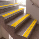 Yellow anti-slip rubber strips installed on concrete stairs, shown in a real stairwell environment with a wall and metal handrail visible.