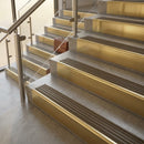 Antique brass stair nosings with dark brown ribbed inserts on stone steps beside a glass balustrade