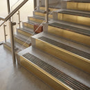 Brass stair nosings with dark bronze ribbed inserts on stone steps beside a glass balustrade