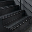 Black anodised nosings blending into charcoal stair treads under low light, with a black handrail above