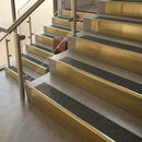 Brass stair nosings with black Olympic grip grit inserts on stone steps beside a glass balustrade