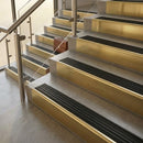Brass stair nosings with black castellated inserts on stone steps beside a glass balustrade