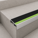 Close-up of an aluminium stair nosing with black and green textured inserts on a pale tiled step edge