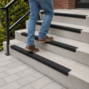 Man descending outdoor concrete steps fitted with black GRP nosings, black handrail and brick wall