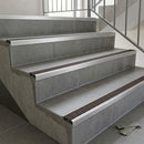 Slimline aluminium stair nosings with dark brown anti-slip inserts on grey tiled staircase