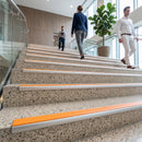 Modern terrazzo stairs with bright orange safety grip strips and silver metal handrails, shown in a bright office lobby with three people walking up the steps.