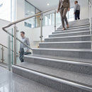 Gray stone stairs with stainless steel handrails in a modern office building, with several people walking up and down the steps.