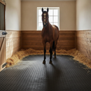Black heavy-duty rubber stable mats covering the floor of a horse loose box with a horse standing on the matting and straw bedding around the edges