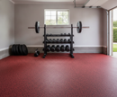 Red rubber gym flooring roll installed in a garage gym beneath a dumbbell rack and loaded barbell