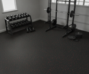 Black rubber gym flooring roll installed wall-to-wall in a home garage gym with a weight rack, dumbbells and barbell