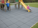 Grey interlocking rubber playground safety tiles installed beneath a climbing frame and yellow slide with children playing
