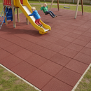 Red interlocking rubber playground safety tiles fitted beneath a slide and swings in a garden play area