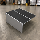 A metal ramp with black textured non-slip pads on a gray concrete warehouse floor.