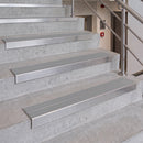 Stainless steel stair nosing strips installed on concrete stairs in an indoor stairwell with a metal handrail.
