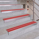 Red and silver metal stair grips installed on concrete stairs with a stainless steel handrail.