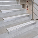White and silver metal stair tread strips installed on concrete stairs next to a stainless steel handrail.
