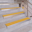 Concrete stair steps with bright yellow textured handrails and silver metal guard rails, shown in an indoor stairwell with a stainless steel handrail post.