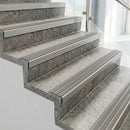 Raked back nosings with flint grey ribbed inserts on pale concrete steps beside a glass balustrade