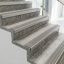 Raked back nosings with flint grey ribbed inserts on pale concrete steps beside a glass balustrade