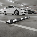 Black and white rubber car park wheel stop bolted down in an underground multi-storey car park with a car parked behind it