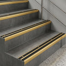 Gold anodised nosings with black anti-slip inserts running along dark grey concrete steps in a stairwell