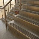 Brass stair nosings with granite brown ribbed inserts on pale stone steps beside a glass balustrade