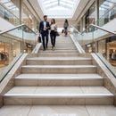 A couple walks up a wide marble staircase in a modern, upscale shopping mall atrium with glass railings and a high ceiling.