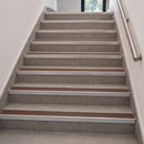 An indoor staircase with gray textured steps, brown horizontal grip strips, silver metal handrails, and white walls.