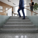 Modern indoor staircase with gray and white speckled terrazzo-style steps and metal handrails, shown in a bright office setting with two people present.