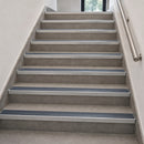 A set of modern interior stairs with textured gray steps and contrasting metallic silver metal rails along the sides.