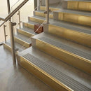 Brass stair nosings with light grey castellated inserts on stone steps beside a glass balustrade