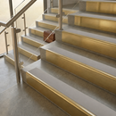 Brass stair nosings with smooth light grey inserts on stone steps beside a glass balustrade