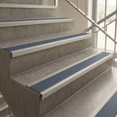 Blue and silver stair tread strips installed on concrete stairs next to a glass railing.