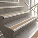 Concrete step stairs with integrated silver metal handrails and tan textured non-slip grip strips on each step, shown in a bright modern interior.