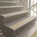 Staircase safety rails with textured beige grip strips installed on concrete steps next to a glass railing.