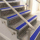 Raked back nosings with mid blue ribbed inserts on mottled stone steps between stainless handrails