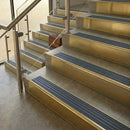 Brass stair nosings with nimbus grey castellated inserts on stone steps beside a glass balustrade