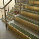 Brass stair nosings with olive green ribbed inserts on stone steps beside a glass balustrade