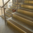 Brass stair nosings with olive castellated inserts on pale stone steps beside a glass balustrade