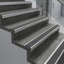 Raked back nosings with black Olympic grip grit inserts on dark concrete steps beside a glass balustrade