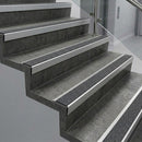 Raked back nosings with black Olympic grip grit inserts on dark concrete steps beside a glass balustrade