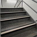 Concrete stair steps with beige non-slip rubber strips and dark metal handrails in an indoor stairwell.