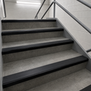 Gray concrete stair steps with black rubber anti-slip strips and a gray metal handrail in a tiled stairwell.
