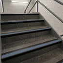 Concrete stair steps with dark metal handrails in an indoor stairwell.