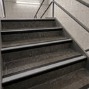 Concrete stair steps with beige non-slip rubber strips and dark metal handrails in an indoor stairwell.