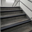 Gray concrete stair steps with black rubber anti-slip strips and a gray metal handrail in a tiled stairwell.