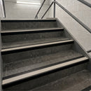 Concrete stair steps with beige non-slip rubber strips and dark metal handrails in an indoor stairwell.