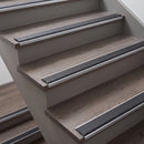 Close-up of indoor stairs with wood-look steps and dark gray non-slip rubber strips along the edges.