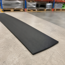 A long, narrow black rectangular mat or strip placed diagonally on a light gray concrete floor, with a blurred warehouse background showing pallets and shelving.