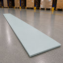 A long, thin rectangular light gray board or panel placed diagonally on a polished warehouse floor, with stacked cardboard boxes and yellow safety posts visible in the blurred background.